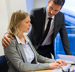 Man with arm on shoulder of woman at computer